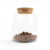 Clear glass jar with cork lid containing expanded clay pebbles on a white background